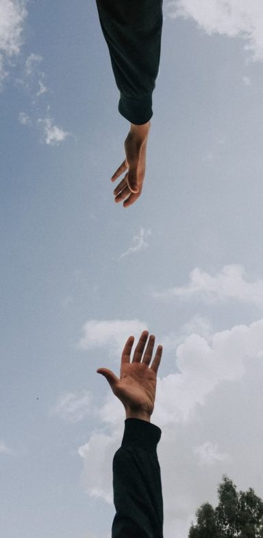Physiotherapie mit Empathie Hände strecken sich einander entgegen vor einem nur leicht bewölkten Himmel.