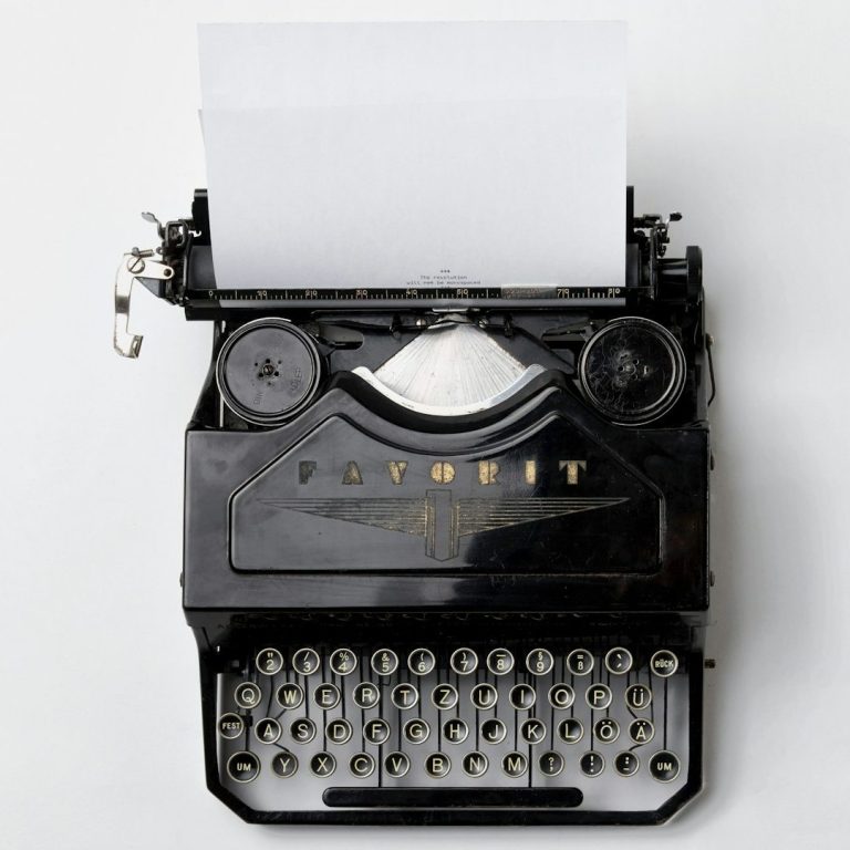 Albert Jakob | Mein Blog Schwarze Schreibmaschine mit weißen Tasten und leerem Blatt Papier.